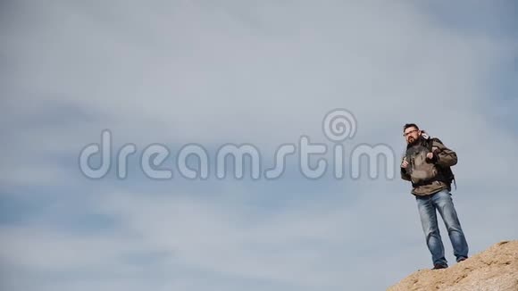 一个年轻人一个旅行者站在高坡上映衬着迷人的天空用他的手机视频的预览图