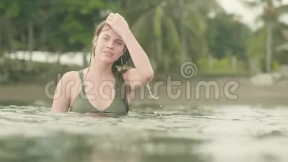 迷人的女人在海上溅水和摆姿势相机微笑的女孩在热带棕榈树的海水中嬉戏视频的预览图