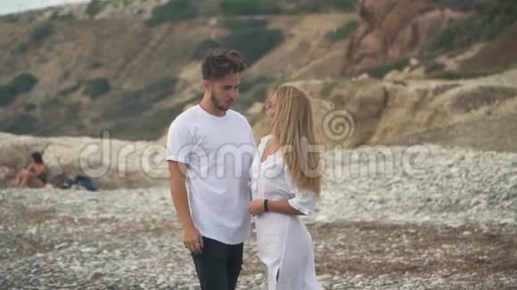 年轻的一对夫妇站在岩石海上说话慢吞吞男人和女人温柔地拥抱在一起他们的头发视频的预览图