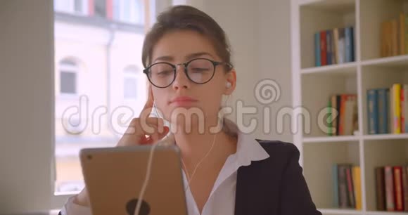 年轻的高加索女商人戴着眼镜在平板电脑上浏览在平板电脑上听音乐的特写镜头视频的预览图