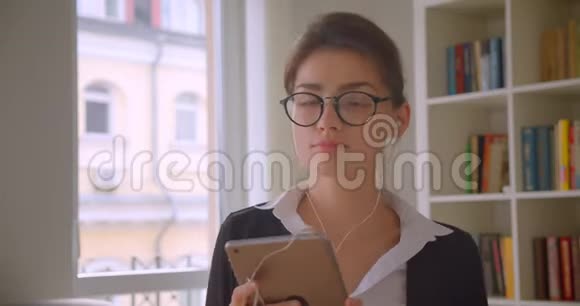 年轻的高加索女商人戴着眼镜在平板电脑上浏览在平板电脑上听音乐的特写镜头视频的预览图