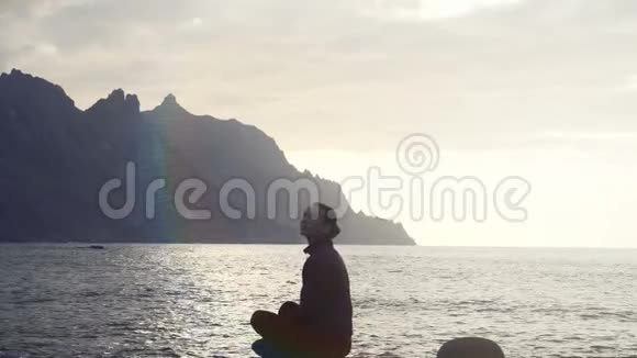 在加那利群岛的特内里费一位妇女坐在岩石上在日落时观察海浪视频的预览图