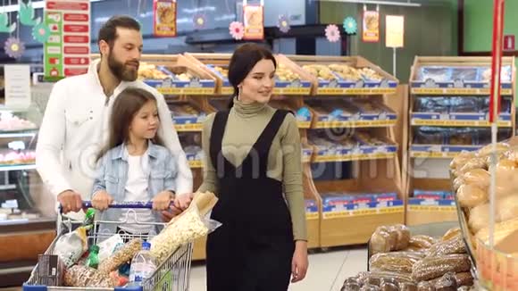 幸福的家庭和小女孩从食品店的货架上挑选面包视频的预览图
