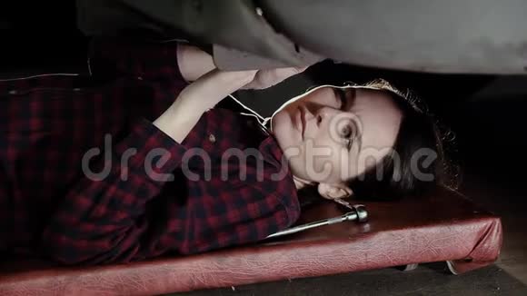 漂亮的女孩一个汽车修理工躺在车下转动螺母视频的预览图