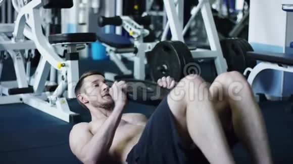 年轻运动员在裸躯干的健身房里用举重练习腹肌视频的预览图