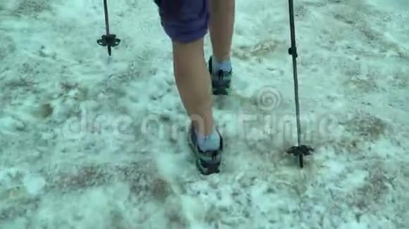 近在脚下的女孩走过春天肮脏的雪在寒冷的颜色一个徒步旅行者用徒步旅行的电线杆爬过春天的雪视频的预览图