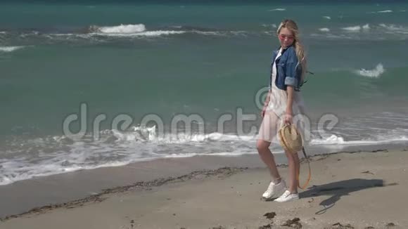 年轻漂亮的女人穿着一件白色透明的裙子白发随风飘扬沿着海滨散步视频的预览图