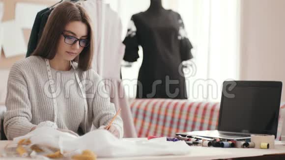 明亮的女孩时装设计师坐在工作室的一张桌子上画画视频的预览图