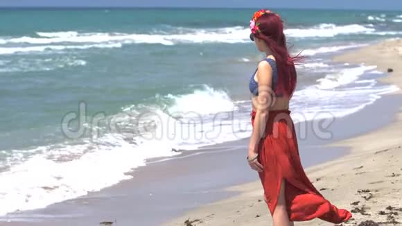 年轻女子穿着红色的裙子和蓝色的上衣红色的头发在风中飘扬看着暴风雨的大海视频的预览图