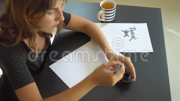 一位年轻女子用刻字技巧在纸上书写书法的特写镜头她写的更多视频的预览图