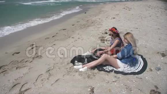 慢动作两个年轻性感的女人和一只狗在沙滩上放松在电话里给她拍照视频的预览图