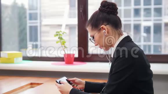 商业概念一个戴耳机的女人用手机上网视频的预览图