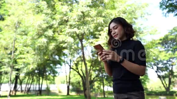 女人在公园里散步和使用智能手机视频的预览图