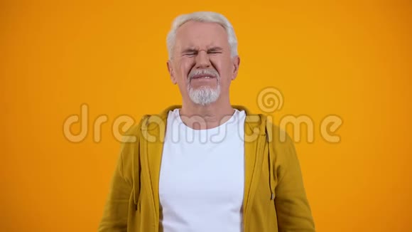 老人用手掌捂住耳朵被流言蜚语激怒背景呈橙色视频的预览图
