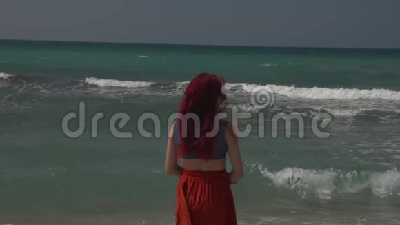 一位戴墨镜的红发年轻女子站在一片海浪中视频的预览图
