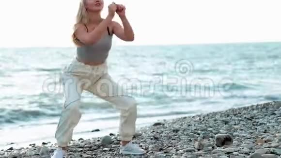 健身年轻女性锻炼核心和臀部与体重锻炼做深蹲运动在海滩上视频的预览图