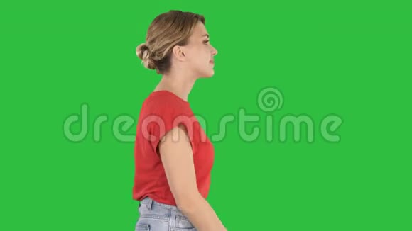穿着牛仔裤和T恤穿在绿色屏幕上的会走路的女人ChromaKey视频的预览图