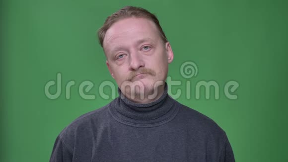 金发中年男子穿着灰色套头衫在绿色的背景上他的头反转着视频的预览图