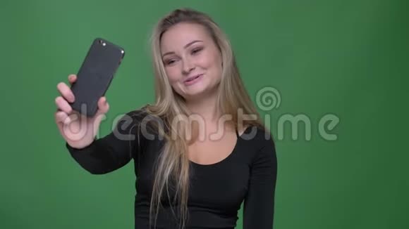 年轻模特穿着黑色上衣的肖像在绿色背景下的智能手机上愉快地在视频聊天视频的预览图