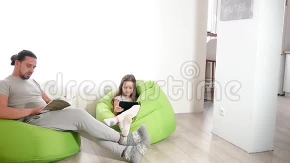 英俊的白人爸爸和一个可爱的女儿坐在椅子上在平板电脑上打电话给Skype神父读视频的预览图