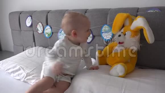 快乐男孩在床上拥抱兔子玩具活泼的男孩和大毛绒兔子在床上玩视频的预览图