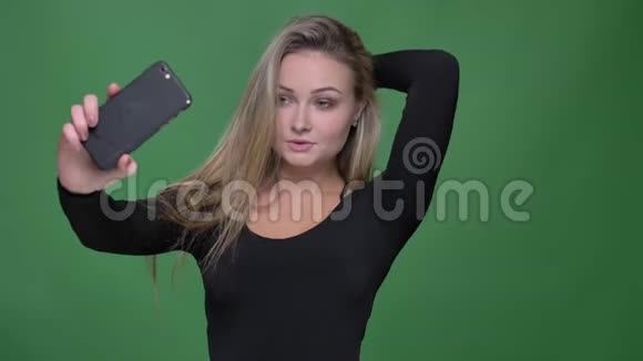 年轻模特穿黑色衬衫的肖像在绿色背景下使用智能手机制作自拍照片视频的预览图