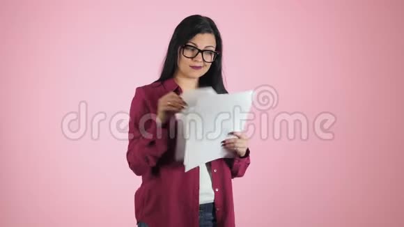 年轻漂亮的黑发女商人戴着眼镜看粉色背景的文件现代严肃的学生认为视频的预览图