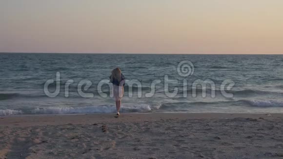 慢动作的金发女郎穿着半透明的连衣裙和牛仔夹克沿着海滨去冲浪视频的预览图
