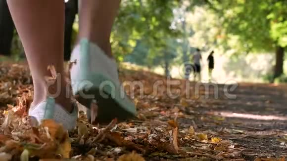 人们在秋天公园散步脚下落叶优雅的女人穿白色短裤金秋概念视频的预览图