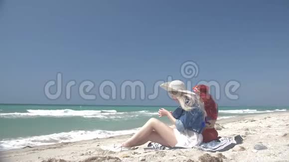 一对穿着波霍风格的年轻性感女人正在沙滩上坐着手机视频的预览图