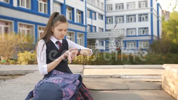 十几岁的女孩坐在学院附近的栏杆上背着一个背包看着他的智能手表视频的预览图