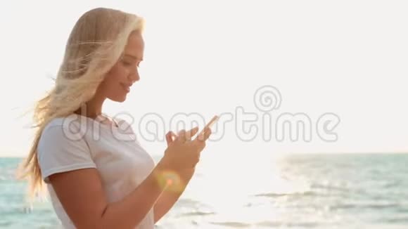 漂亮的少女在海滩上使用智能手机背景是大海和地平线视频的预览图