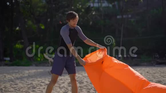 一个年轻人在热带海滩上的超慢镜头使充气沙发充气暑假概念视频的预览图