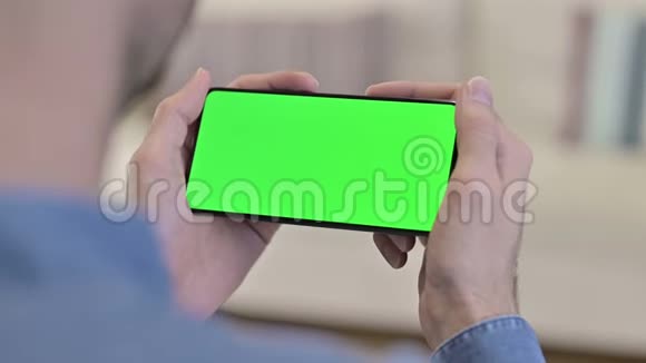 男子在绿色模拟屏幕智能手机上观看视频视频的预览图