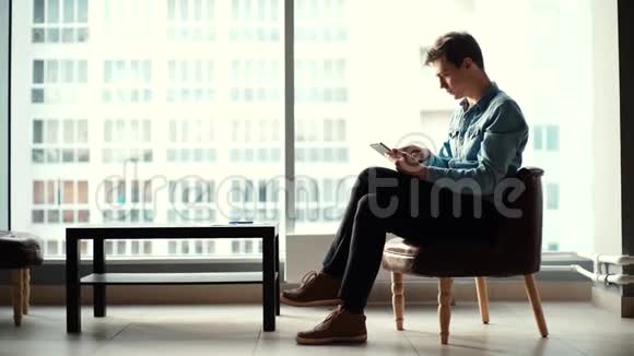 英俊的年轻商人坐在椅子上在办公室里用平板电脑视频的预览图