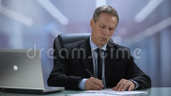公司老板带笔记本电脑在办公桌上阅读和签署文件视频的预览图