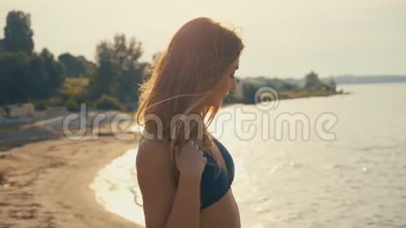性感的年轻女人穿着比基尼在海滩上日落时摆姿势视频的预览图