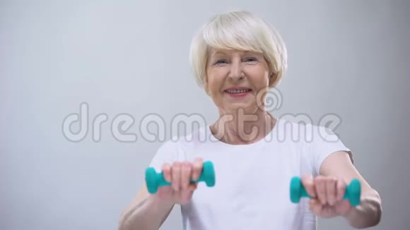 戴着哑铃对着镜头微笑的老年女性健康健康的生活方式视频的预览图
