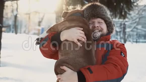 在冬天阳光明媚的日子里快乐的长胡子的拥抱他的斗牛犬友谊圣诞节冬天宠物的概念视频的预览图