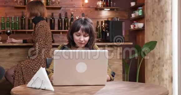 一个漂亮的女孩在咖啡店喝咖啡的时候在电脑上打字视频的预览图