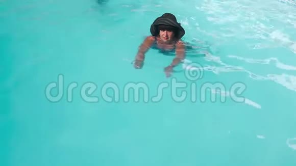 戴着黑帽子的白人老年女性在酒店的蓝色游泳池游泳娱乐的概念视频的预览图