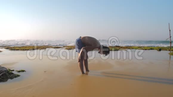 盖伊在沙滩上伸展抵御海浪的冲击视频的预览图