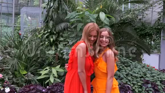 两个穿着鲜艳裙子的女孩在植物园摆姿势视频的预览图