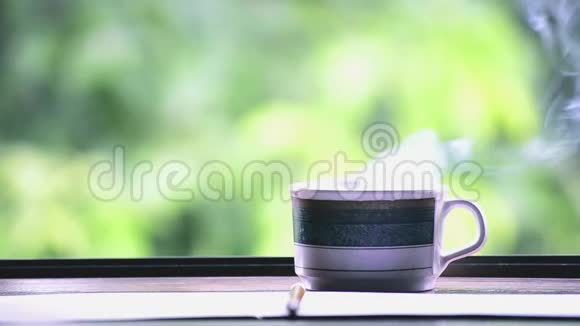 餐桌上的热咖啡模糊的绿叶景观自然背景上的阳光视频的预览图
