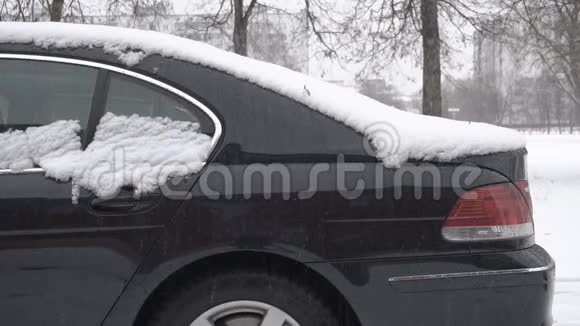 冬天雪落在站在街道上的现代黑色汽车上视频的预览图