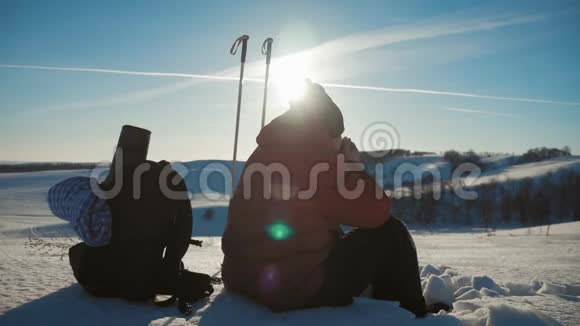 人类旅行者坐在冬天的山上的悬崖上喝热水瓶里的茶年轻人的后景视频的预览图