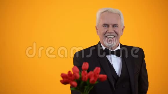 一位年长的绅士带着郁金香花束微笑着真诚地迎接节日视频的预览图
