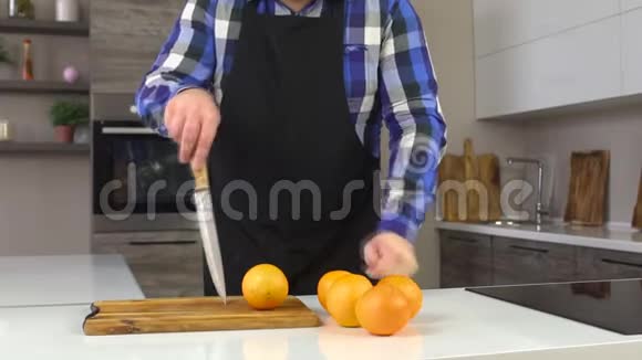 一个穿围裙的男人在厨房里切橘子维生素特写慢动作背景视频的预览图