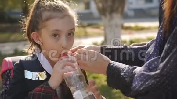 穿校服的小女孩喝塑料瓶里的水母亲调整女儿的领带女孩就松开了视频的预览图