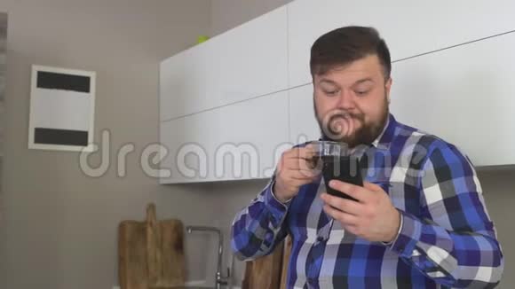 一个留着胡子的人正在现代化的厨房里喝咖啡慢慢地在手机里浏览新闻视频的预览图